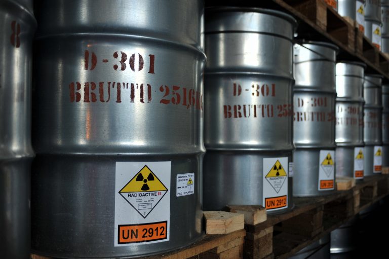 A row of labelled cylindrical barrels, labelled as radioactive and containing yellowcake.