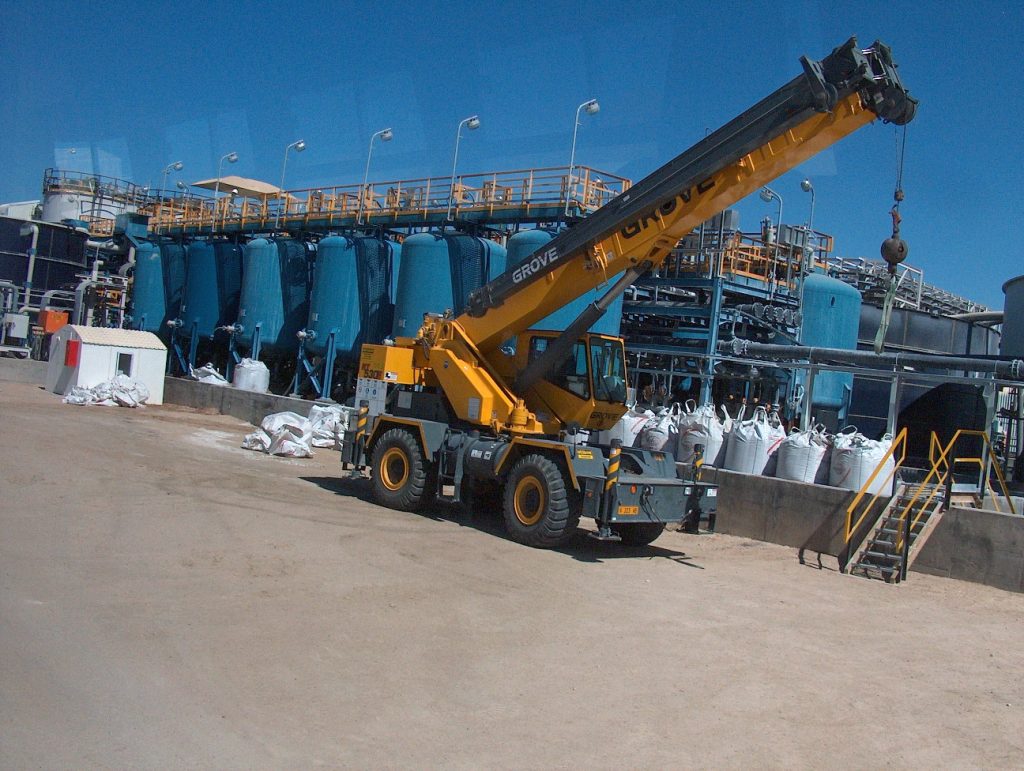 A large yellow mining truck transports extracted earth at an open-pit uranium mining site under a clear blue sky, showcasing the scale of modern mining operations.