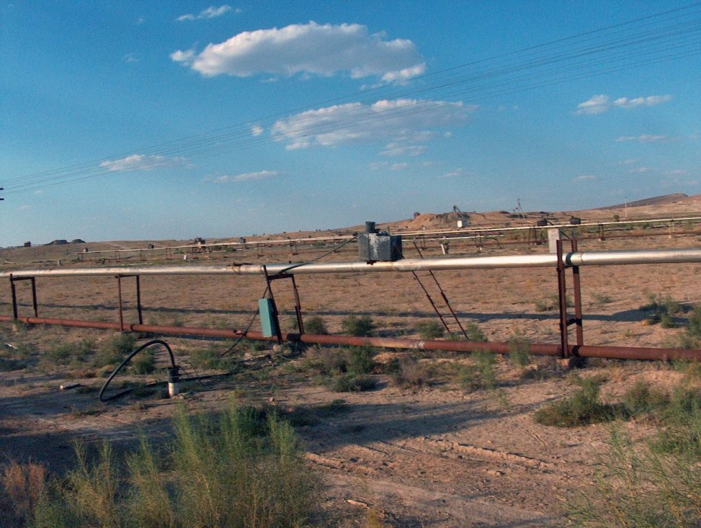 A wide view of an open-pit uranium mine with terraced layers carved into the earth, surrounded by arid landscape and industrial equipment in the distance.