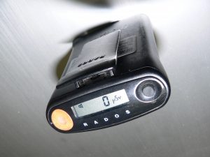 An Electronic Personal Dosimeter (EPD) with a clip to attach to the wearer. Shown is the EPD's electronic readout, indicating a dose of 0 μSv.