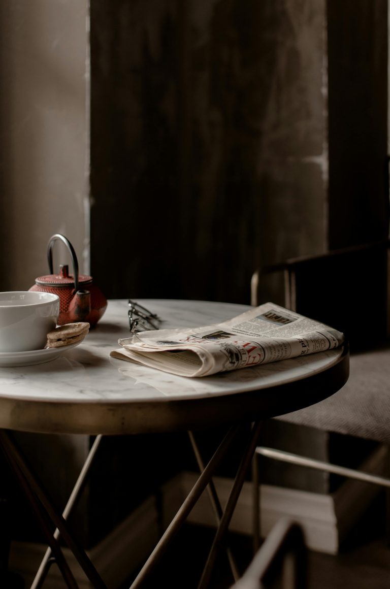 A newspaper lying on a table next to a pot of tea