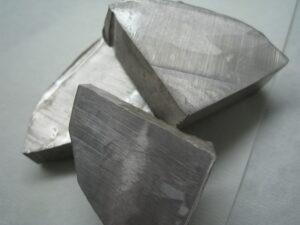 Three irregular, silvery-white lumps of sodium metal with a slightly dull, oxidized surface, placed on a non-reactive surface in a lab setting.