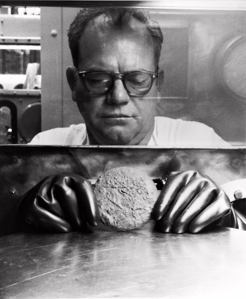 A worker holding a Plutonium 'button' inside a glovebox.